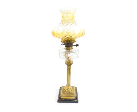 A brass Corinthian column oil lamp, with a faceted cut clear glass reservoir, on a canted square base embossed with flowers, 