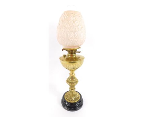A brass oil lamp, of fluted baluster form, raised on black glass socle, with chimney and a pink opaline molded floral and fol