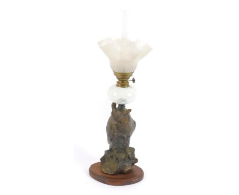 A cast metal oil lamp, modeled as an owl perched on a bough, raised on a wooden base, with clear and opalescent glass reservo