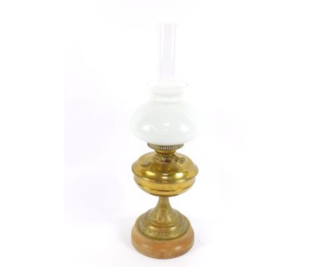 A duplex brass oil lamp, of baluster form, the stem embossed with flowers and leaves, on a wooden socle, with chimney and whi