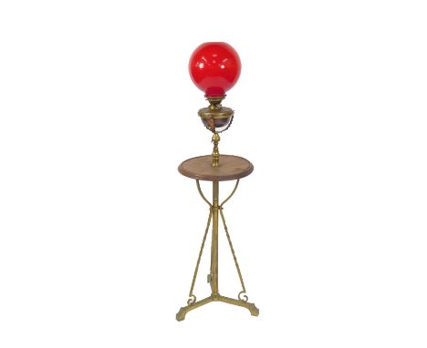 A Hinks's standard telescopic oil lamp, with a circular wooden table centre, raised on a tripod base, with red glass shade, 1