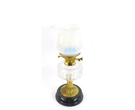 A brass oil lamp, with a fasted clear cut glass reservoir, raised on a black glass socle, with chimney and opalescent glass s
