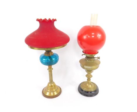 A brass oil lamp, raised on a black glass circular socle, with red globular glass shade, 57cm high, together with a further b