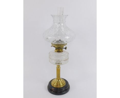 A brass oil lamp, with a faceted clear cut glass reservoir, raised on a circular black glass socle, with chimney and clear ho