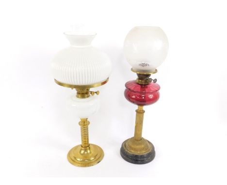 A brass fluted column oil lamp, with a cranberry glass reservoir, raised on a black circular socle base, with an etched globu
