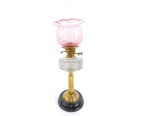 A fluted brass oil lamp, with a faceted clear glass reservoir, raised on an embossed circular base and black glass socle, wit