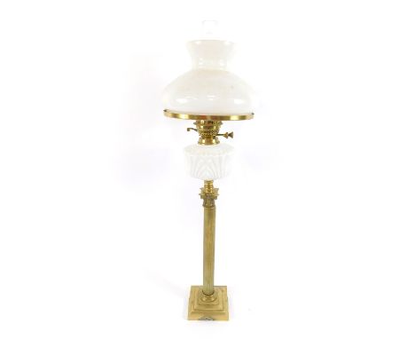 A brass Corinthian column oil lamp, raised on a stepped square base, with a white molded glass reservoir, brass fittings, wit