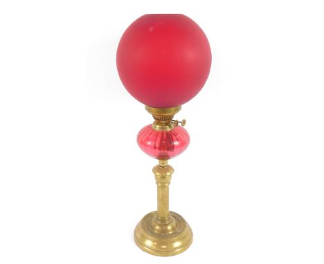 A brass oil lamp, raised on a circular base, with a fluted cranberry glass reservoir, with chimney and frosted red glass shad
