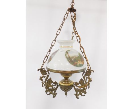 A brass hanging oil lamp, cast with hunting figures and foliate scrolls, with a white glass shade, printed with three landsca