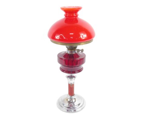 A chrome and red painted oil lamp, with a ruby glass reservoir, with chimney and red glass shade, 66cm high.