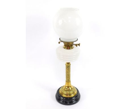 A brass Gothic style oil lamp, with a white glass reservoir, raised on a circular black glass socle, with a white globular gl
