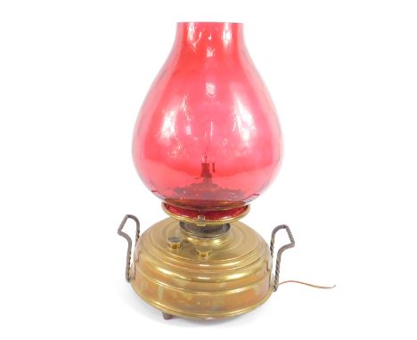 A brass burner oil lamp, with cast iron carrying handles, converted to electricity, with a cranberry honeycomb glass shade, 5