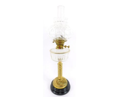 A brass spiral fluted oil lamp, with a cut clear glass reservoir, raised on a black glass socle, with glass chimney and clear