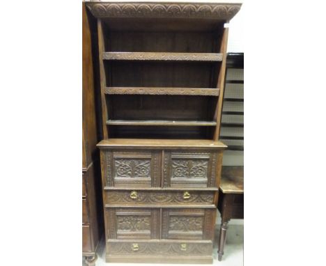 An oak and carved bookcase cabinet with three open shelves over two pairs of cupboard doors and two drawers on a plinth base