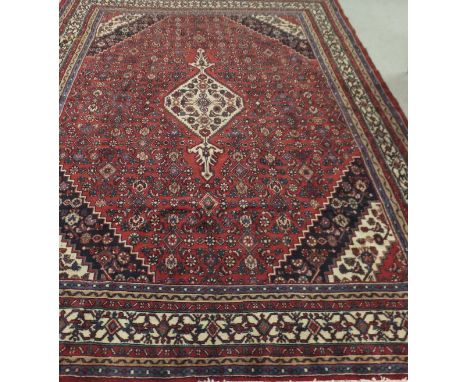 A Hamadan carpet, the central medallions in cream, blue and red on a red motif decorated ground within red, cream, blue, gree