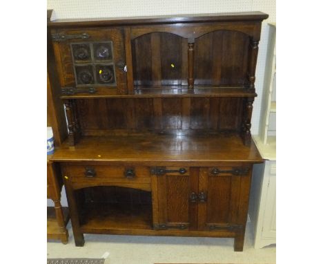 An oak dresser in the Arts and Crafts manner, the top with single glazed cupboard and bullseye glass beside a plate shelf abo