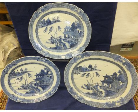 A graduated set of three 19th Century Chinese blue and white platters, the centre fields decorated with waterside dwelling wi