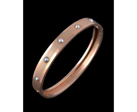  An early 20th century French gold and pearl bracelet,   circa 1900, the hinged bangle set with five half pearls, on a stippl