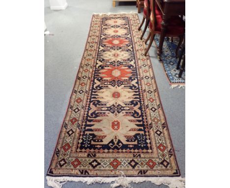 A KAZAK STYLE RUNNER woven with seven cruciform alternating medallions on a dark blue ground, 340cm x 100cm, supplied by Iran
