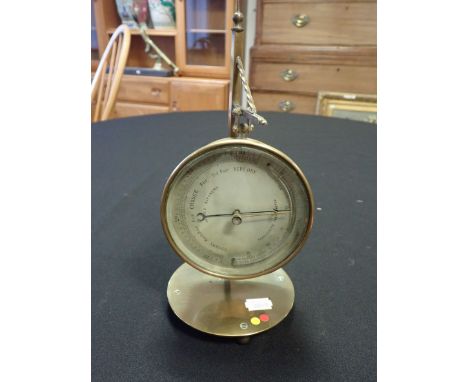 A VICTORIAN BRASS CIRCULAR ANEROID BAROMETER with silvered dial, on stand with circular base, 27 cm high