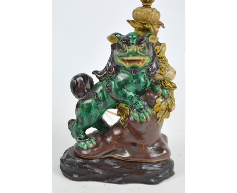 A ceramic lamp base modelled as a green temple lion upon a rock surrounded by flowers and foliage on a wooden base, height ex