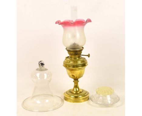 A late 19th century brass oil lamp with pink tinted shade above a part gadrooned reservoir and circular foot, height includin