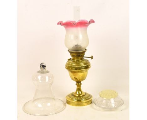 A late 19th century brass oil lamp with pink tinted shade above a part gadrooned reservoir and circular foot, height includin