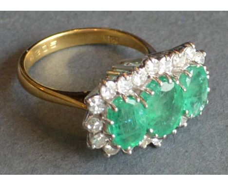 An 18ct. Yellow Gold, Emerald and Diamond Ring Set with three oval emeralds surrounded by diamonds within a pierced setting 