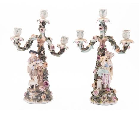 A pair of Sitzendorf porcelain candelabra each modelled with a figure stood before a flower encrusted stump supporting three 