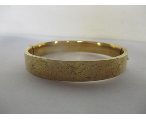A 9ct gold bangle with and floral and scrolls engraved decoration. 13.6g 