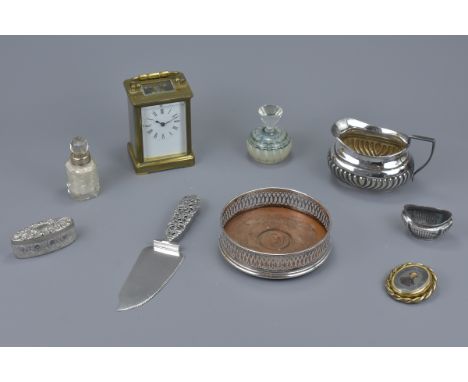 A carriage clock together with a silver plated wine bottle coaster, milk jug, cake slice, glass scent bottle, two pots and a 