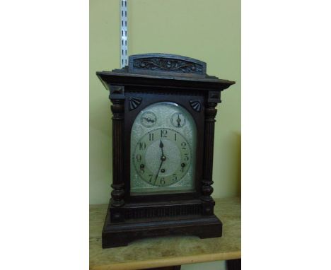 An Edwardian oak bracket clock, the case with turned and fluted columns and carved detail, enclosing an arched silvered dial 
