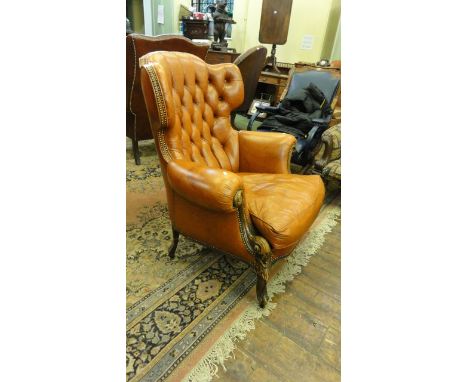 A flamboyant Georgian style upholstered armchair with scrolled arms and winged back upholstered in a light tan leather with b