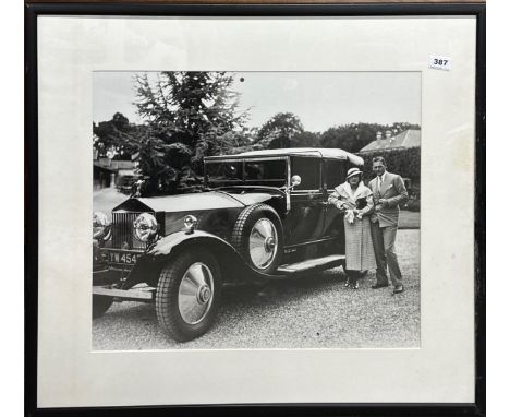 A large framed photographic print of a couple standing beside an early motorcar, frame size 74 x 84cm. Slight damage to frame
