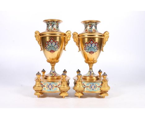 Pair of French gilt metal and enamel clock garniture supporting vases of urn shape with mask handles, raised on vase shaped s