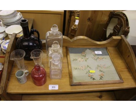 A quantity of various glass bottles and a small needlework tapestry 