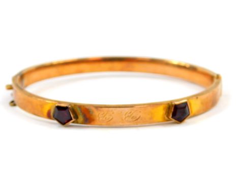 A 9ct gold bangle, set with two pentagonal garnets, initialled BB, on a snap clasp, safety chain lacking, 7.6g.