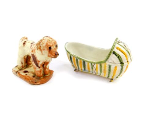 A Staffordshire early 19thC pearl ware cradle, 10cm wide, together with a slip ware figure of a dog, modelled standing on a o