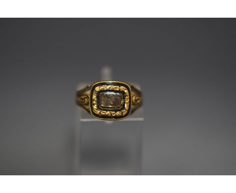 A George IV mourning ring, the glazed hair panel enclosed by chasing and black enamel, to a trifurcated enamelled shank, insc