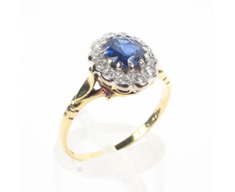 An 18ct  yellow and white gold cluster ring. Principally set with an oval cut sapphire weighing approximately 0.70ct and surr