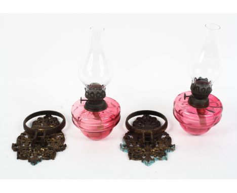 A pair of Victorian gilt-metal mounted cranberry glass wall mounted oil lamps, each pierced mount cast with a vase amongst sc