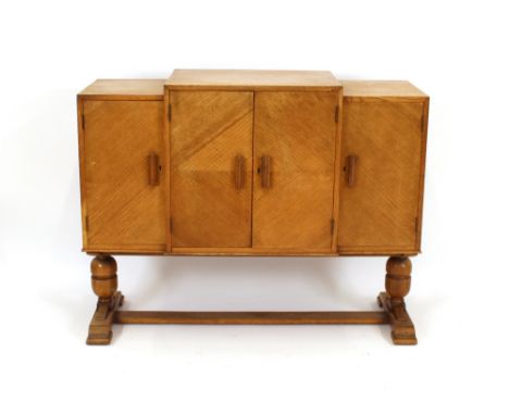 An Art Deco light oak sideboard, of breakfront form enclosed by four doors and raised on cup and cover supports, 123cm wide