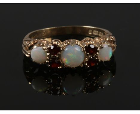 A 9ct gold, opal and garnet ring with scroll formed shank. Size L.  