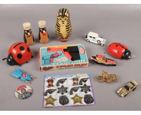 A box of toys including a retro toys spud gun in original packaging, Russian doll and Japanese tin pate sheriff badges in ori