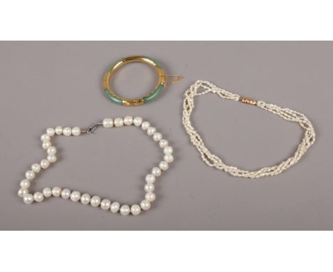Two strings of pearls, one with 14ct gold clasp, along with a jade coloured hardstone and yellow metal bangle.  