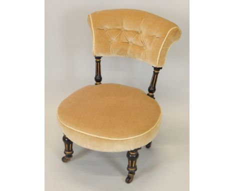 A Victorian ebonised and parcel gilt nursing chair, with a padded back and seat, on turned legs with ceramic castors