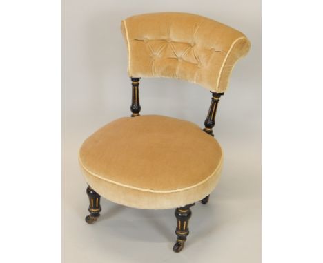 A Victorian ebonised and parcel gilt nursing chair, with a padded back and seat, on turned legs with ceramic castors