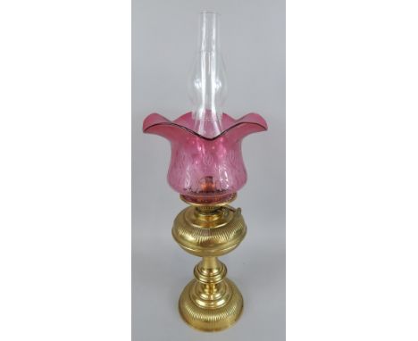A Victorian brass lamp base, with Art Nouveau style cranberry tinted shade, a clear glass chimney, 54cm high and an extra sma
