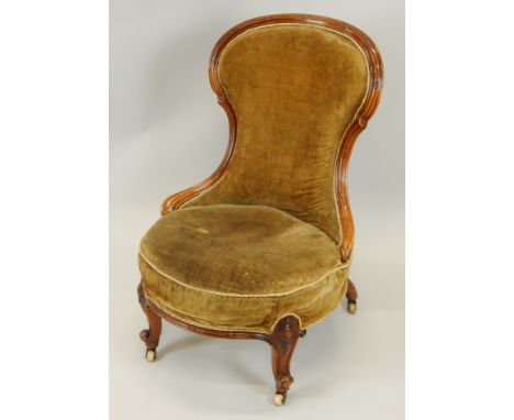 A Victorian walnut show-frame nursing chair, with a padded back and seat, on cabriole legs with ceramic castors