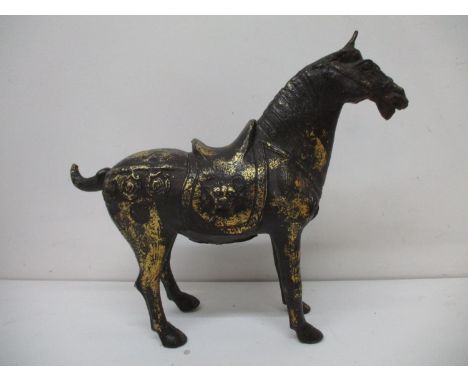 A 20th century brown patinated and gilt cast iron model of a Tang horse with a saddle and harness, decorated with animal mask